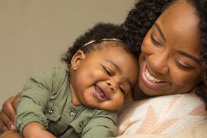 Woman smiles while holding smiling infant close to her chest.
