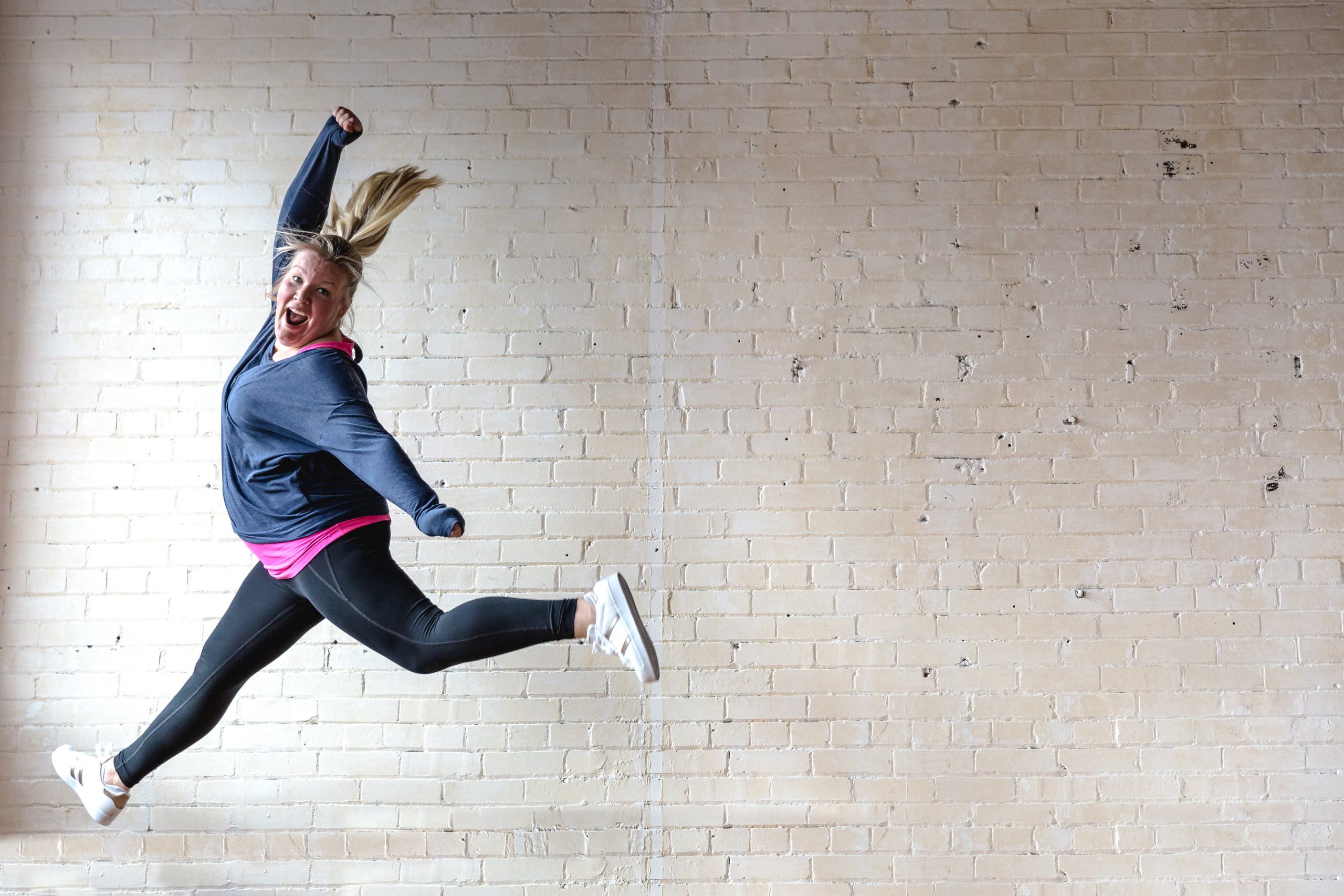 woman in athletic wear leaping, white brick background