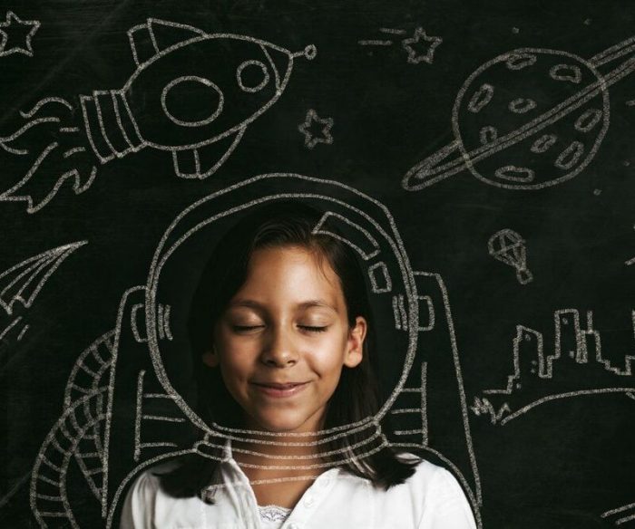 Young girl with her eyes closed, smiling against a chalk board filled with drawings of space exploration