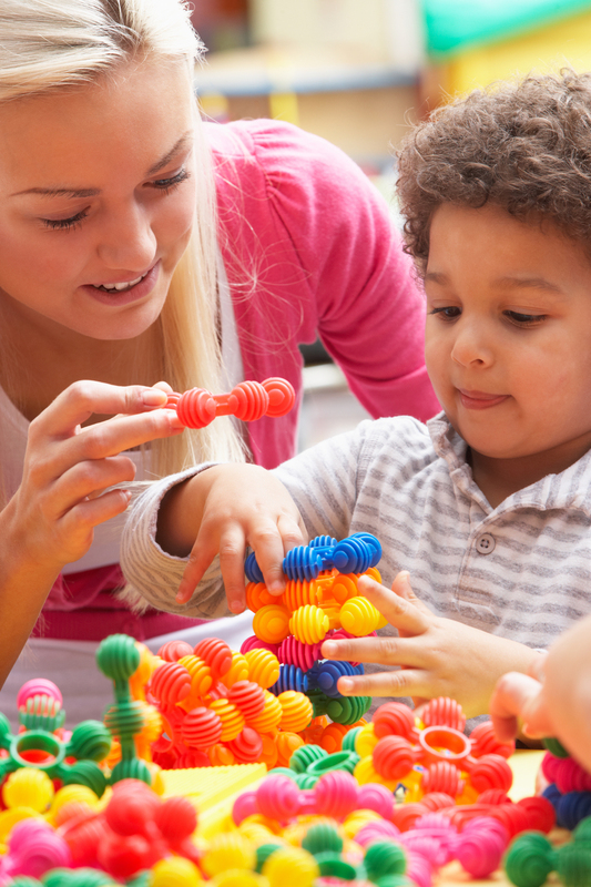 teacher helps small boy play with colourful plastic toys