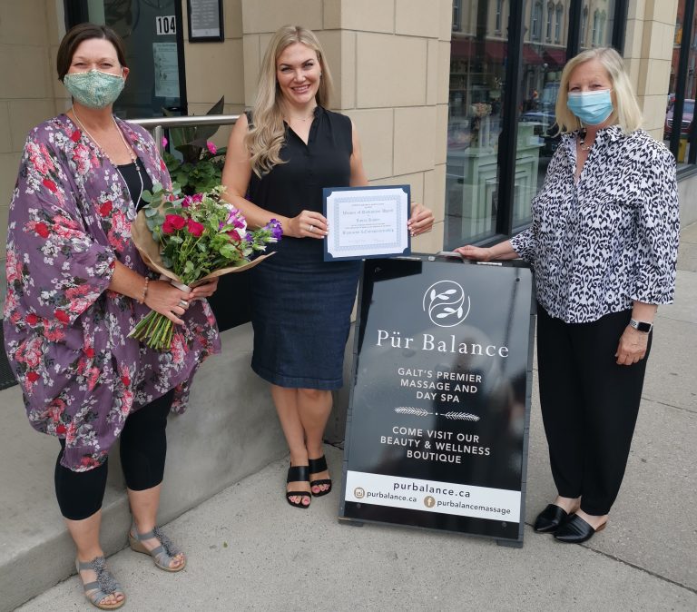 Women standing in front of "Pur Balance" sign holding certificate and flowers.