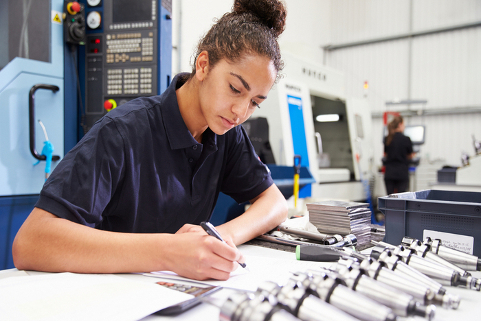 woman writes notes at desk in a trades or technical work setting