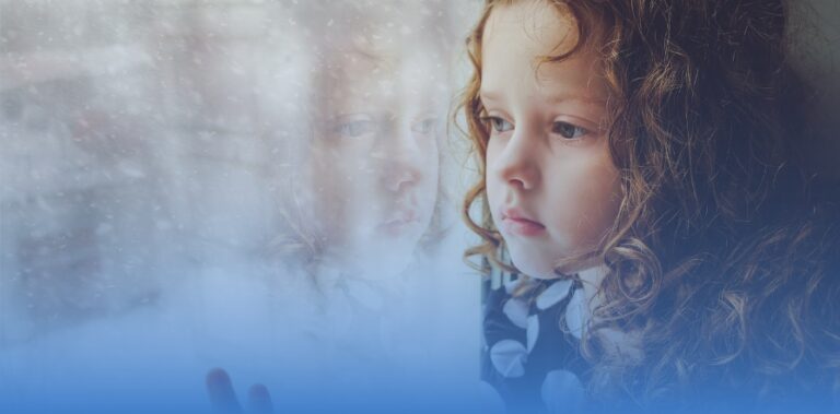 Photo of a young girl looking sadly out a window. Blue ombre overlay.