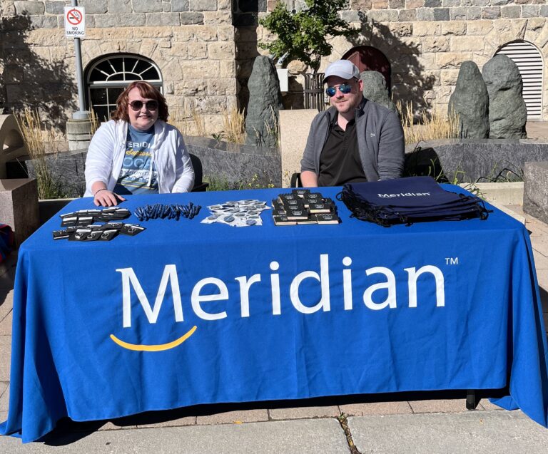 Two people behind table with blue tablecloth that says "Meridian".