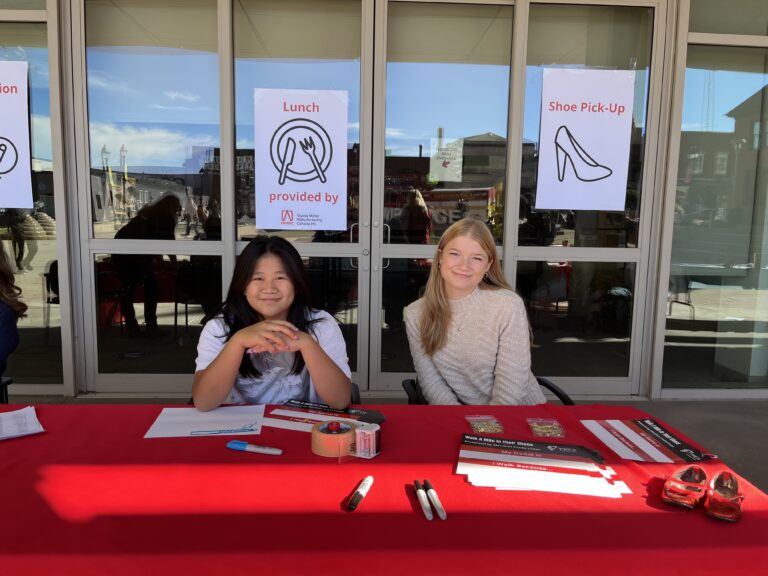 Two young women smiling behind table at "walk a mile in her shoes"