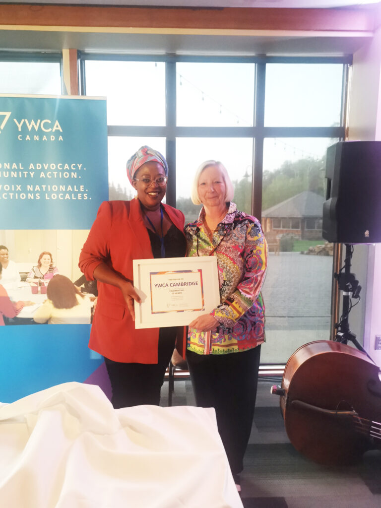 Kim Decker stands with Aline Nizigama; they're holding a plaque recognizing YWCA Cambridge's 75 years of service