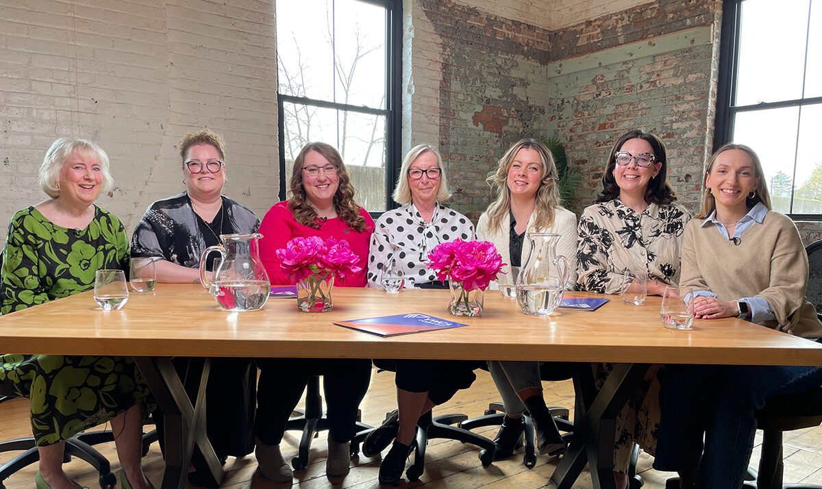 The YWCA Cambridge leadership team sits around a large wood table, facing the camera and smiling