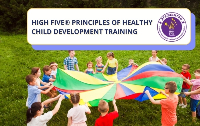 Children play the big parachute game. Title of training event top right.