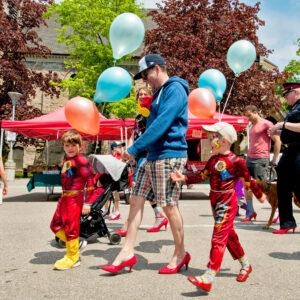 Man in red high heels and children walking to end gender based violence.