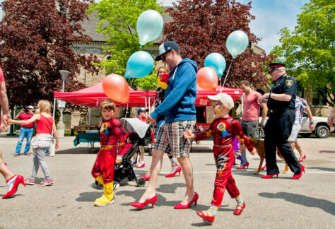 Man in red high heels and children walking to end gender based violence.