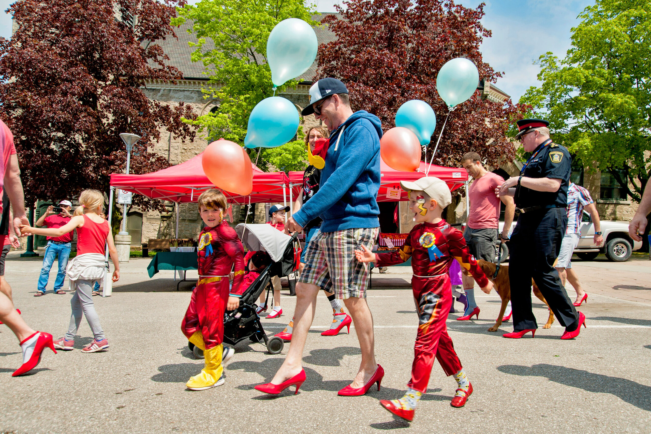 Man in red high heels and children walking to end gender based violence.