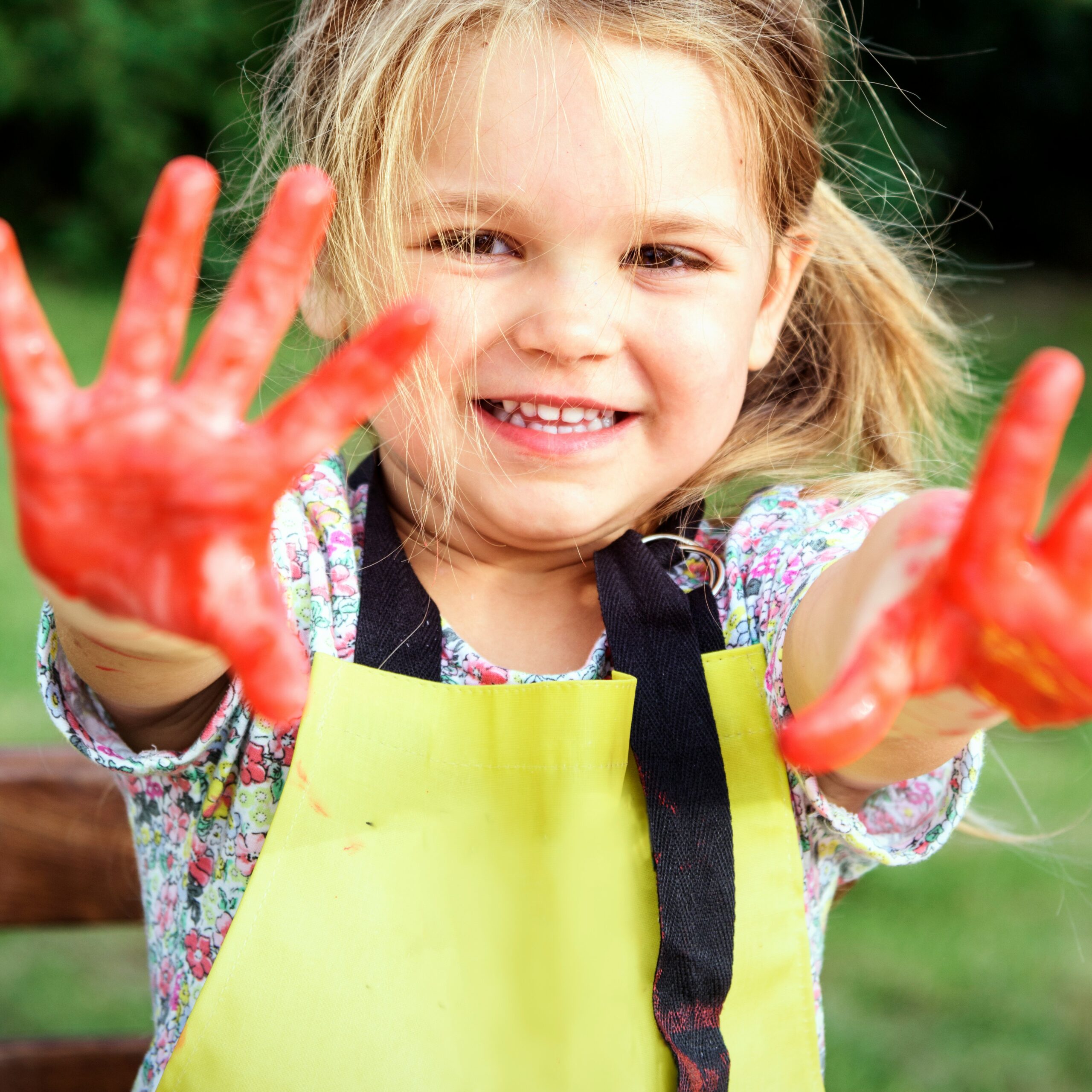 A young girl smiles with red paint on her hands