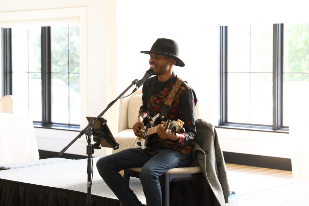 a guitar musician in a large hat sits in front of a stage