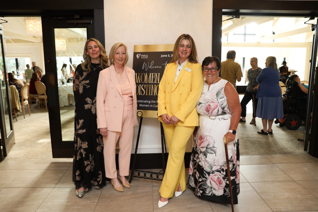four women stand in front of the women of distinction welcome sign in front of the event space.