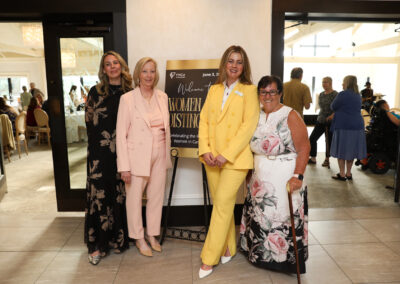 four women stand in front of the women of distinction welcome sign in front of the event space.