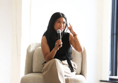 a woman speaks into a microphone while seated on a beige chair