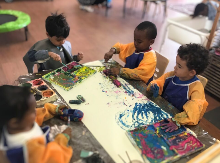 children gather around an art table for a painting activity