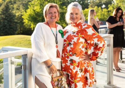 two formally dressed women stand on a deck that backs onto a golf course