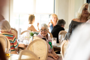 many people seated at gala tables, and one woman with bold glasses observes the room