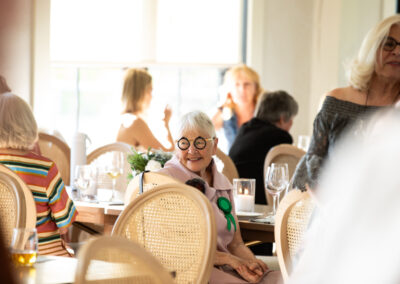 many people seated at gala tables, and one woman with bold glasses observes the room