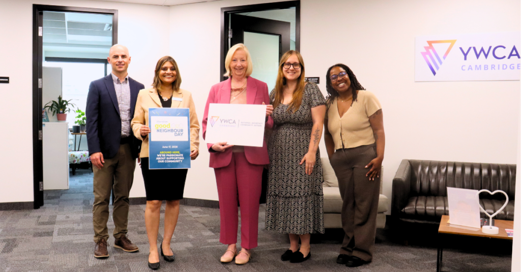 five people stand in an office holding signs during the Good Neighbour Day tour of YWCA Cambridge’s head office.