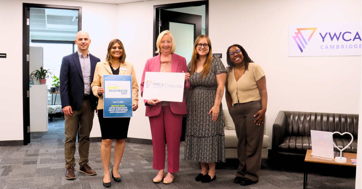 five people stand in an office holding signs during the Good Neighbour Day tour of YWCA Cambridge’s head office.