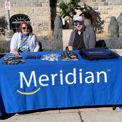 Two people behind table with blue tablecloth that says "Meridian".